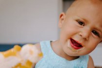 Милый маленький ребенок смотрит в камеру с грязным ртом наслаждаясь вкусным домашним фруктовым мороженым во время отдыха на террасе — стоковое фото