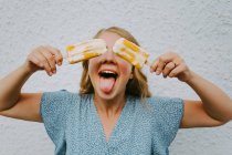 Feminino fazendo careta engraçada com língua para fora e cobrindo os olhos com saborosos piruetas de gelo em paus — Fotografia de Stock