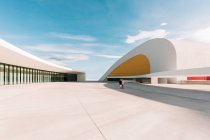 Außenseite des Auditoriums mit weiß-gelben geschwungenen Wänden auf dem weißen Betonplatz des Oscar Niemeyer International Cultural Centre vor wolkenlosem blauem Himmel an sonnigen Tagen in Spanien — Stockfoto