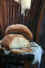 Loafs de sabroso pan y cuchillo afilado colocado en un pedazo de tela en una silla de madera - foto de stock