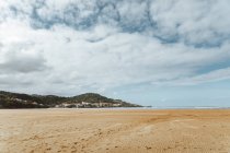 Calm sandy coast during low tide and green hills with buildings — Stock Photo