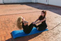 Hochwinkelseitenansicht einer reifen Frau mit kleiner Tochter, die Asana im Sitzen macht, während sie gemeinsam Partner-Yoga auf der sonnigen Dachterrasse praktiziert — Stockfoto