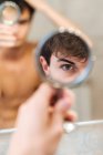 Серьезный мужчина, стоящий в светлой ванной комнате и смотрящий в круглое зеркало утром — стоковое фото