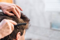 Crop Mann Bürsten der Haare von jungen Kerl und dabei Frisur im hellen Badezimmer — Stockfoto