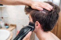Männchen mit Haarschneider schneiden Haare von Kerl in zeitgenössischem Badezimmer zu Hause — Stockfoto