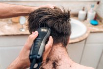 Hombre con recortadora de cabello corte de pelo de chico en el baño contemporáneo en casa - foto de stock