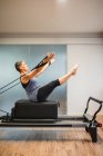 Seitenansicht einer erwachsenen Frau in Sportbekleidung, die auf einem Pilates-Gerät liegt und Übungen mit Widerstandsbändern macht — Stockfoto
