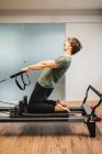 Side view of sportsman in activewear using pilates machine and stretching arms with resistance bands — Stock Photo