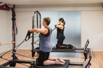 Vista lateral de atletas focados em activewear fazendo exercícios na máquina pilates e bombeando músculos com equipamentos de resistência metálica — Fotografia de Stock