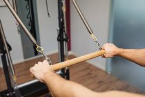 Unerkennbarer männlicher Athlet beim Training mit hölzerner horizontaler Stange des Pilates-Reformators in modernem Fitnessstudio — Stockfoto