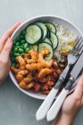 Top view of cropped unrecognizable person holding white poke bowl with rice and cucumber with beans and mushrooms topped with shrimps — Stock Photo