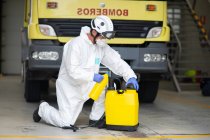 Side view of fireman in protective costume and respirator pouring liquid in plastic container for disinfection of fire station during coronavirus pandemic — Stock Photo