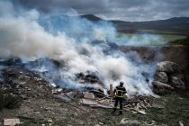 Visão traseira do bravo bombeiro em uniforme protetor em pé com mangueira e extinguindo o fogo no despejo nas montanhas — Fotografia de Stock