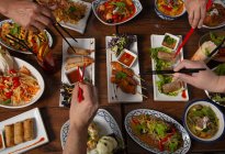 Blick von oben auf würziges thailändisches Essen, serviert auf Holztisch, Hände mit Essstäbchen — Stockfoto