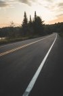 Estrada de asfalto que vai perto do lago pacífico e da floresta verde contra o céu nublado do pôr do sol no Parque Nacional La Mauricie, em Quebec, Canadá — Fotografia de Stock