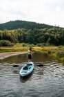 Rückansicht einer unkenntlichen Reisenden mit Kajak, die im sauberen Wasser des Flusses steht und den grünen Hügel im La Mauricie Nationalpark in Quebec, Kanada bewundert — Stockfoto
