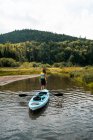 Visão traseira de viajante feminino irreconhecível com caiaque em pé na água limpa do rio e admirando a colina verde no Parque Nacional La Mauricie em Quebec, Canadá — Fotografia de Stock