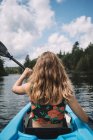 Back view of anonymous female traveler in life vest sitting in boat during river exploration against cloudy sky in La Mauricie National Park in Quebec, Canada — Stock Photo