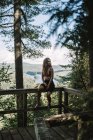 Ganzkörper junge Touristinnen sitzen auf dem Geländer einer Holzterrasse und schauen weg im Wald des La Mauricie Nationalparks in Quebec, Kanada — Stockfoto