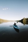 Silhouette of anonymous female traveler sitting on kayak and rowing during trip on calm river on cloudless day in La Mauricie National Park in Quebec, Canada — Stock Photo