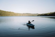 Silhouette of anonymous female traveler sitting on kayak and rowing during trip on calm river on cloudless day in La Mauricie National Park in Quebec, Canada — Stock Photo