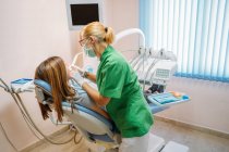 Focalisé médecin professionnel d'âge moyen en uniforme vert examinant la cavité buccale de la femme dans la chaise dentiste — Photo de stock