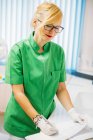 Focused adult woman in glasses and uniform working in dental hospital and writing on paper card at table — Stock Photo