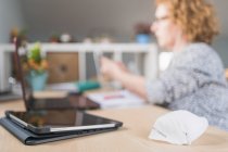 Seitenansicht einer erwachsenen Frau in Freizeitkleidung und Brille mit Smartphone im Kopfhörer, während sie am Tisch sitzt und zu Hause am Laptop arbeitet — Stockfoto