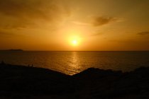 Pittoresco paesaggio marino con sagome di persone che camminano sulla riva del mare vuota durante il tramonto della sera a Ibiza — Foto stock