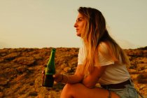 Junge Frau mit Flasche Bier bei Sonnenuntergang am Strand — Stockfoto