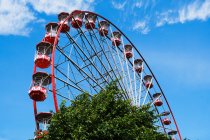 Dal basso della ruota panoramica con cabine rosse situate sul parco divertimenti con alberi e torre nelle giornate di sole con cielo azzurro — Foto stock