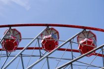 From below of Ferris wheel with red cabins located on amusement park on sunny day with blue sky — Stock Photo