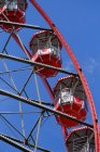 From below of Ferris wheel with red cabins located on amusement park on sunny day with blue sky — Stock Photo
