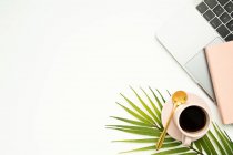 Vista superior del espacio de trabajo creativo con netbook y taza de café espresso caliente colocado en la hoja de palma - foto de stock