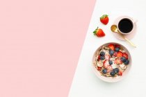Вид сверху на миску для завтрака с вкусными мюсли и ягодами, выставленными на стол с чашкой кофе и свежей клубникой — стоковое фото