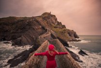 Vista posteriore di turista donna irriconoscibile in abiti caldi a piedi verso ponte cappella durante il viaggio sull'isola di San Juan de Gaztelugatxe in Spagna — Foto stock