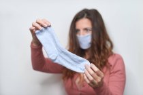 Femme adulte aux cheveux bruns portant un masque respiratoire fait à la main en chaussette bleue pendant la période de quarantaine de pandémie de coronavirus — Photo de stock