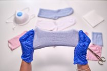 Зверху анонімні люди в синіх стерильних рукавичках показують, як зробити маску для обличчя, використовуючи шкарпетки, перебуваючи вдома під час періоду коронавірусу — стокове фото