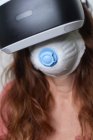 Femme anonyme aux cheveux roux utilisant un masque facial tout en expérimentant la réalité virtuelle en utilisant un casque moderne pendant la période de quarantaine du coronavirus — Photo de stock