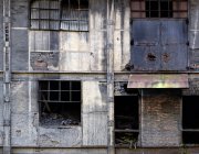 Extérieur du bâtiment industriel en pierre abandonnée avec des fenêtres étroites avec grille métallique et verre cassé — Photo de stock