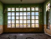 Stanza vuota con pavimento disordinato e ampia finestra con barre metalliche nel vecchio edificio industriale abbandonato — Foto stock