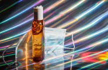 Medizinische Gesichtsmaske und eine Flasche braunes Desinfektionsgel auf holographischem Hintergrund — Stockfoto
