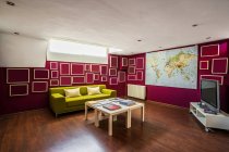 Modernes geräumiges Wohnzimmer mit Holzboden, mit hellgrünem Sofa ausgestattet und mit geometrischen Elementen an roten Wänden dekoriert — Stockfoto
