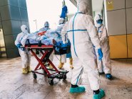 Vista posterior del grupo anónimo de médicos profesionales en trajes de protección que transportan al paciente con infección por virus al hospital - foto de stock