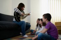 Fröhliche Frau spielt daheim im Wohnzimmer Gitarre für Kinder — Stockfoto