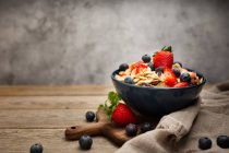 From above delicious breakfast bowl of corn flakes with strawberries and blueberries placed on cutting board and decorated with linen cloth and berries around dish on wooden table with gray background — Stock Photo