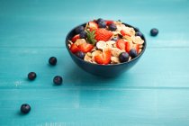 Du dessus délicieux bol de petit déjeuner de flocons de maïs avec des fraises et des bleuets placés sur la planche à découper et décoré avec du linge de maison et des baies autour du plat sur fond bleu bois — Photo de stock