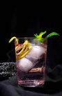 Cóctel de Gin tonic con agua tónica rosa, pimienta rosa, romero, menta, canela, limón y naranja sobre fondo oscuro - foto de stock