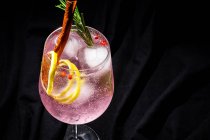 Джин тоник коктейль с розовой тонизирующей водой, розовый перец, розмарин, мята, корица, лимон и апельсин на темном фоне — стоковое фото