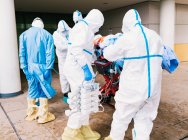 Зворотній бік анонімної групи професійних лікарів у захисних костюмах, що перевозять пацієнта з вірусною інфекцією до лікарні — стокове фото
